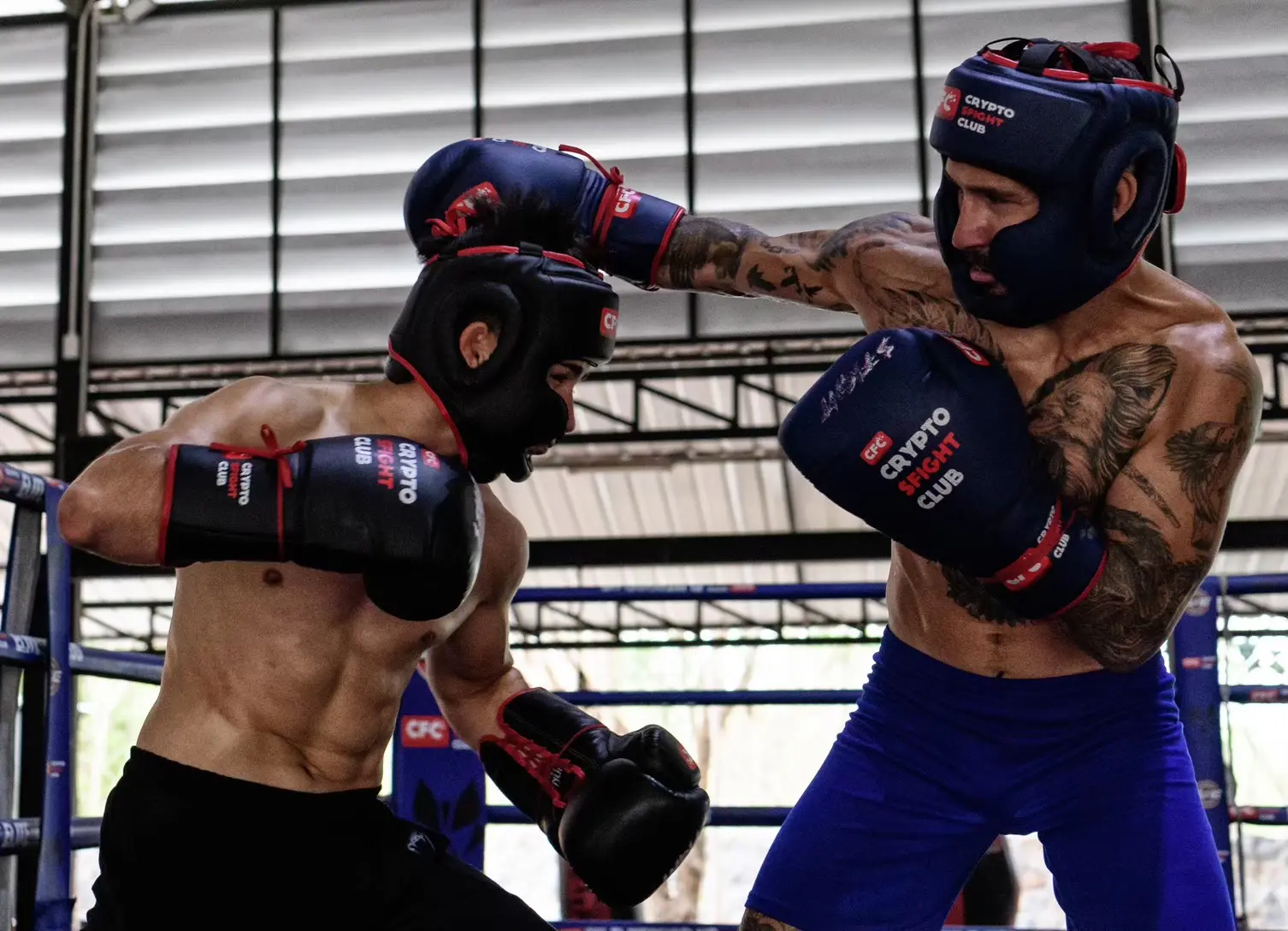 Sparring sur le ring du camp : deux boxeurs casqués échangent des coups.