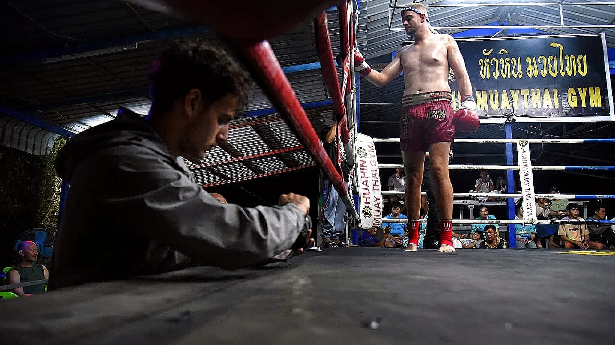 Soir de combat au Hua Hin Muay Thai Gym : un participant attend dans son coin, son coach penché sur le bord du ring.